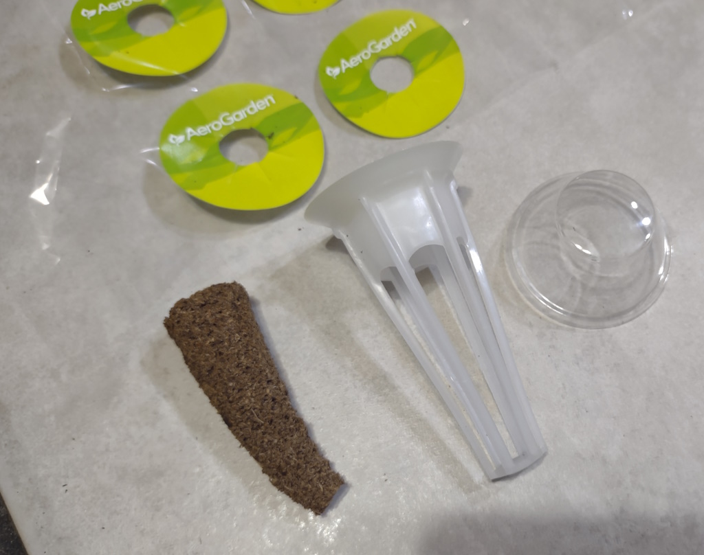 Sample of items included in the AeroGarden Grow Anywhere Kit, being stickers, a grow sponge, a pod, and a cover