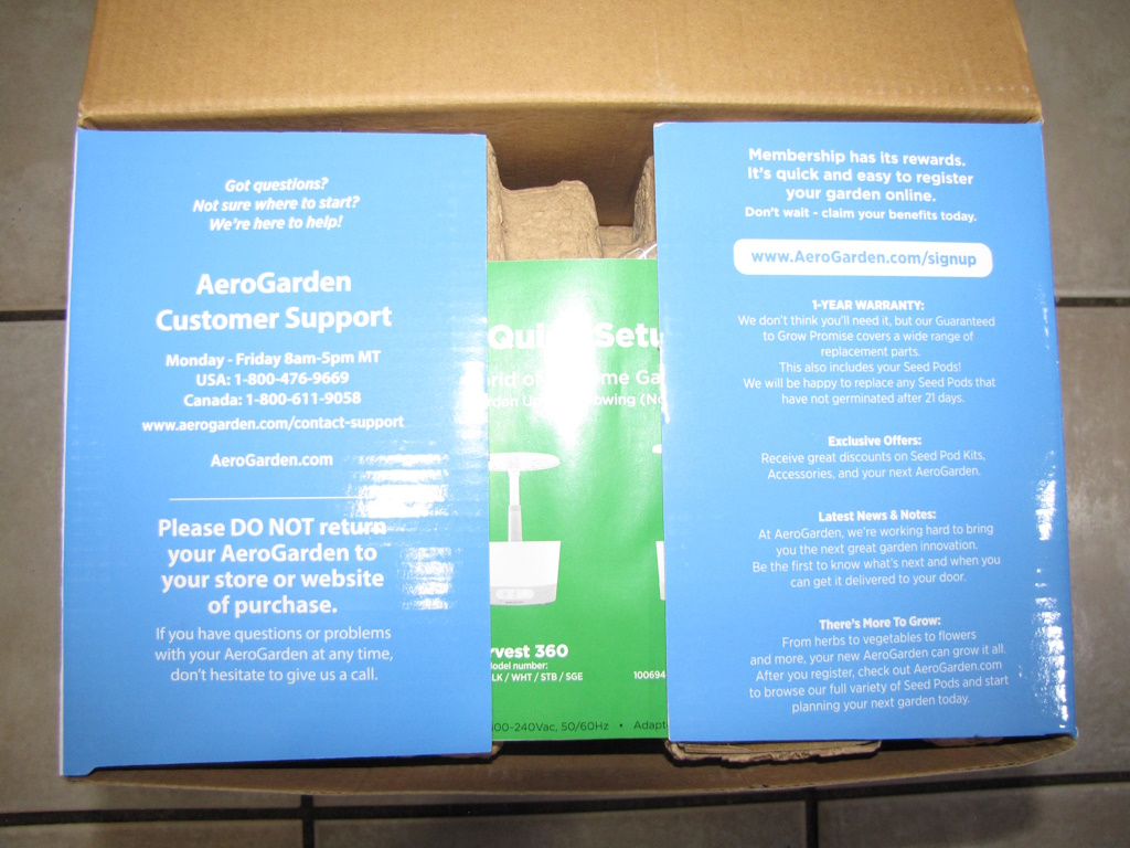 First view of the AeroGarden Harvest box contents showing two blue flaps and a green booklet