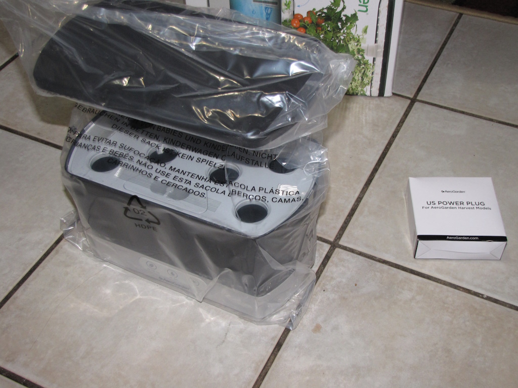AeroGarden Harvest still in its original plastic wrap next to a small box containing the power plug