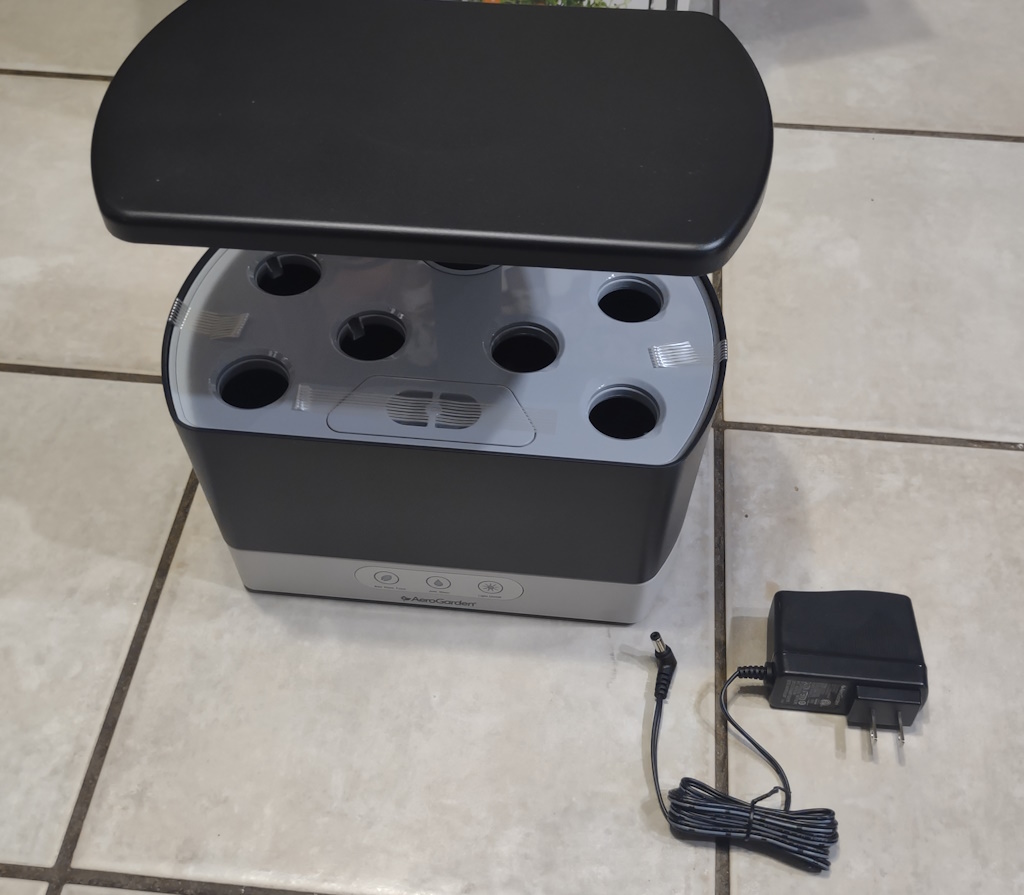 New AeroGarden Harvest with tape still holding tray to tub, next to its power supply with cord still wrapped up